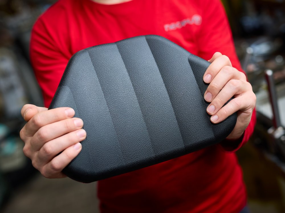 Person h&auml;lt ein schwarzes Integralschaum-Bauteil mit strukturierter Oberfl&auml;che in den H&auml;nden