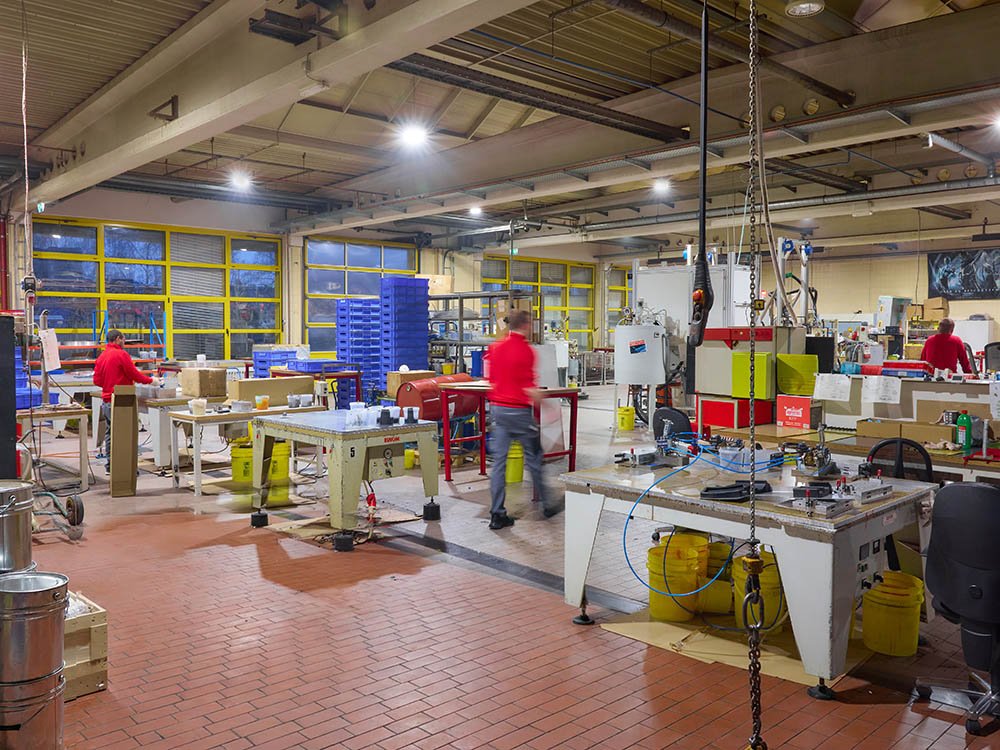 Produktionshalle mit Maschinen, Arbeitspl&auml;tzen und Mitarbeitern im laufenden Betrieb