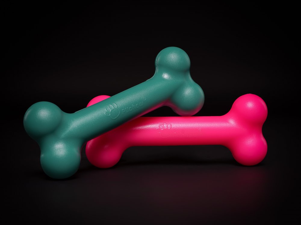 PUchew Hundekauspielzeug in Knochenform in Gr&uuml;n und Pink vor schwarzem Hintergrund