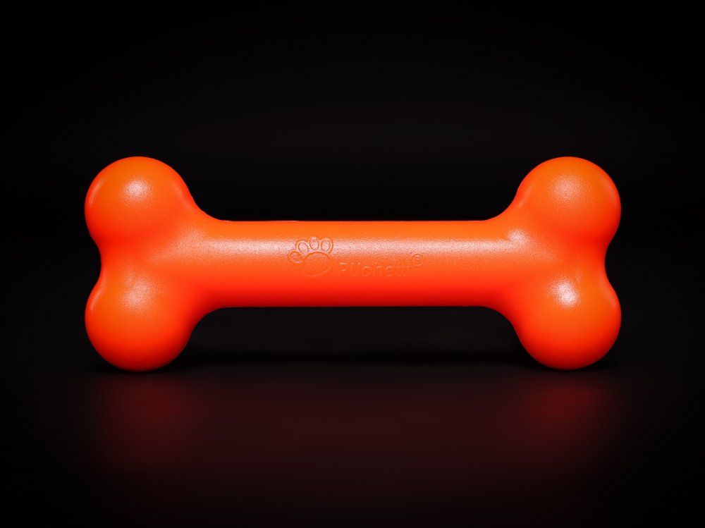 Oranges PUchew Hundekauspielzeug in Knochenform vor schwarzem Hintergrund